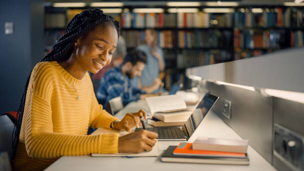 universitätsbibliothek: gifted black girl verwendet laptop, schreibt notizen für das papier, essay, studie für klassenaufgabe. vielfältige multiethnische gruppe von studenten lernen, studieren für prüfungen, gespräch im college - multi ethnic group reading stock-fotos und bilder