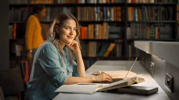 istock University Library: Focused Bright Caucasian Girl Works on Assignment, Use Computer, Looking at the Camera and Smiles. Cute Smart Girl with Autnehtic Individuality 1248521810
