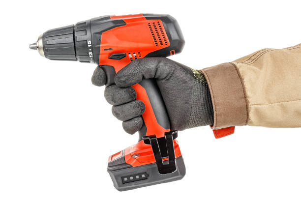 istock Contemporary red cordless drill in worker hand in black protective glove and brown uniform isolated on white background 1248524588