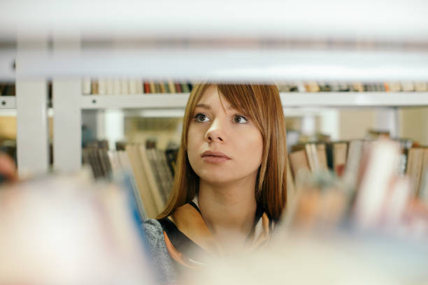 Student, shelf and choice for books in library for research, studying and exam preparation. Woman, novel and search for information with learning, university knowledge and education thesis at college