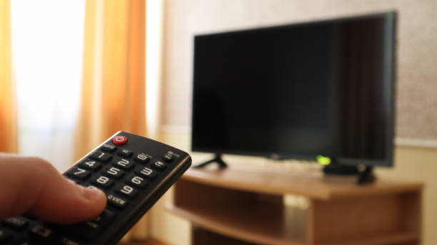 istock Hand holding a television remote control and surfing programs on television. watch, turn on or off the TV in the living room or bedroom on the black-screen nightstand. Copy space 1248529746