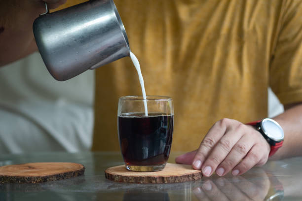 istock Milk pouring from a small pitcher by a man's hand from above into glass with black coffee. 1248531223