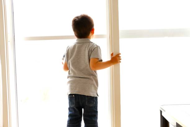 istock Little boy looking outside through the window 1248540886