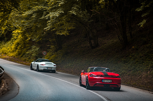 Porsches driving in the group on the open mountain road. Different models are on the photo, from the 911,944, 993 and Boxter models. This photo represent enthusiast driving during weekend and enjoying in mountain road and ride. Photo have vintage look and was taken on the cloudy day.