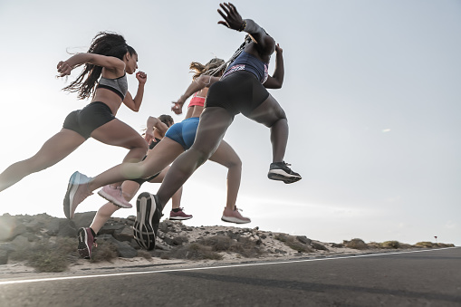 Low angle of powerful multiracial friends in sportswear running fast against evening sky during outdoor workout in outskirts