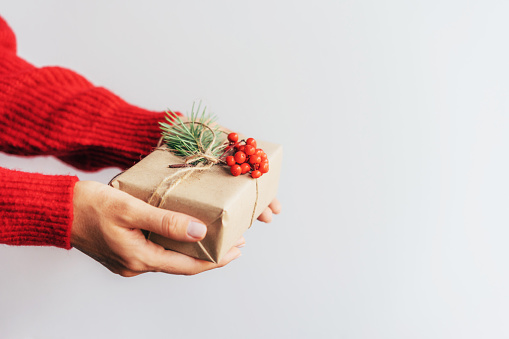A small Christmas present box decorated with red rowan berries in female hands. Place for text. Gift giving. Mercy and charity. New Year concept.