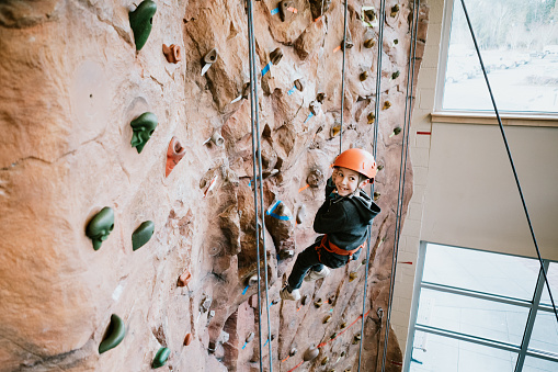 A Caucasian boy climbs a large bouldering  wall at a rock climbing gym.  A fun and healthy way to stay active and physically fit.  Shot in Washington state, USA.