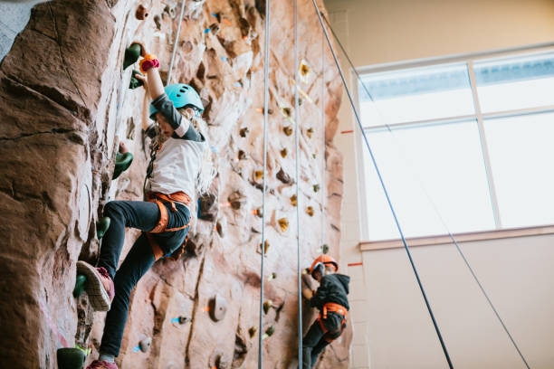 Children Climbing Indoor Rock Wall Boys and girls climb a large bouldering  wall at a rock climbing gym.  A fun and healthy way to stay active and physically fit.  Shot in Washington State, USA. crag stock pictures, royalty-free photos & images
