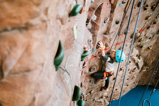 A Caucasian girl climbs a large bouldering  wall at a rock climbing gym.  A fun and healthy way to stay active and physically fit.  Shot in Washington state, USA.