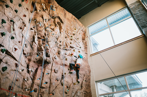 A Caucasian girl climbs a large bouldering  wall at a rock climbing gym.  A fun and healthy way to stay active and physically fit.  Shot in Washington state, USA.