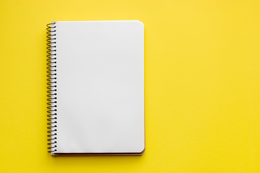 Cuaderno espiral con hojas blancas vacías en blanco sobre un fondo amarillo brillante, vista superior, plano yacía con espacio de copia photo