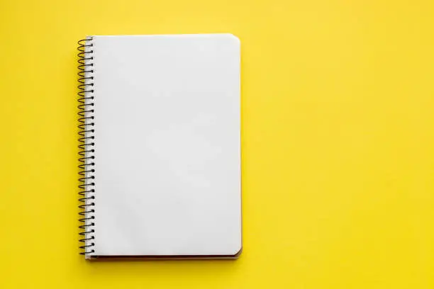 Spiral notebook with blank empty white sheets on a bright yellow background, top view, flat lay with copy space