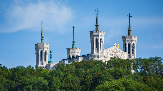 Distant view of famous Basilica Notre Dame de Fourviere on Fourviere hill on the riverbank of Saone river. Taken during a sunny summer day from a boat sailing on Saone river, in the beautiful French city of Lyon, Rhone department in Auvergne-Rhone-Alpes region in France, Europe.