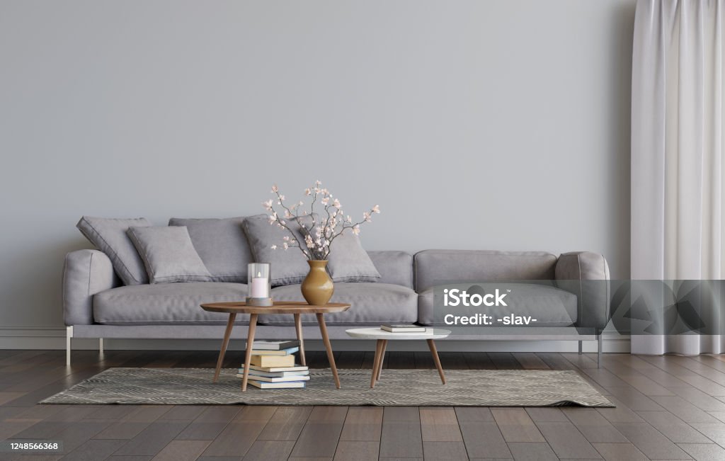 Living room interior with grey sofa and two coffee tables on the carpet.. Empty gray wall mockup. 3D render. Living room interior with grey sofa and two coffee tables on the carpet. Empty gray wall mockup. A pile of books on the carpet, a candle and flowers on the table. 3D render. 3D illustration. Living Room Stock Photo