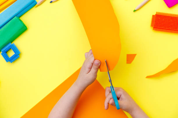 ребенок резки цветной оранжевой бумаги с ножницами на столе для некоторых ремесла - nobody craftwork equipment pencil стоковые фото и изображения