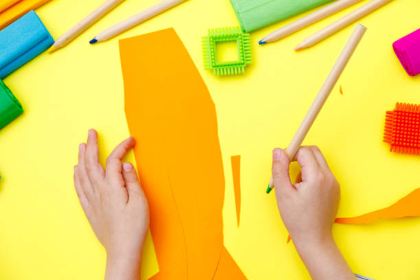 istock Child cutting coloured orange paper with scissors  on a table for some craftwork 1248569406
