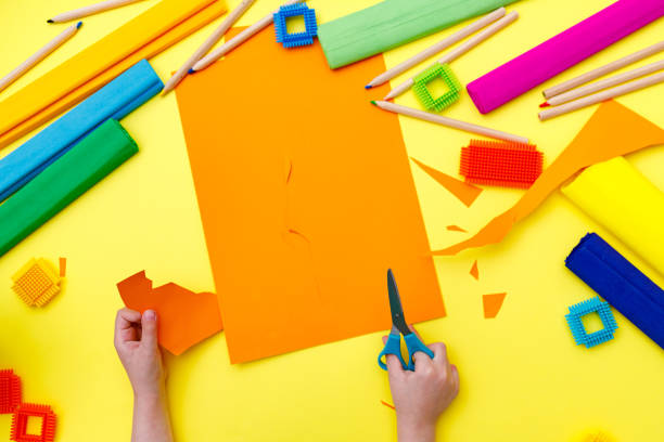istock Child cutting coloured orange paper with scissors  on a table for some craftwork 1248569414
