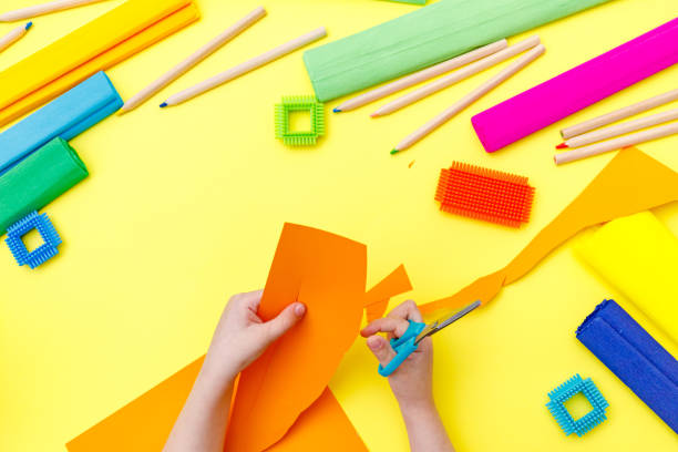 istock Child cutting coloured orange paper with scissors  on a table for some craftwork 1248569441