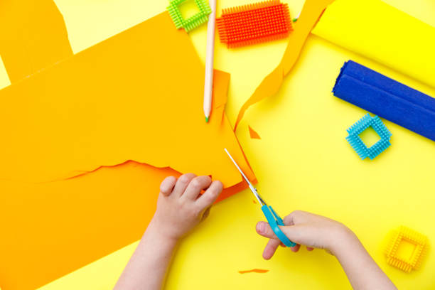 istock Child cutting coloured orange paper with scissors  on a table for some craftwork 1248569443