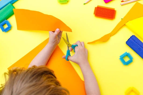 istock Child cutting coloured orange paper with scissors  on a table for some craftwork 1248569451