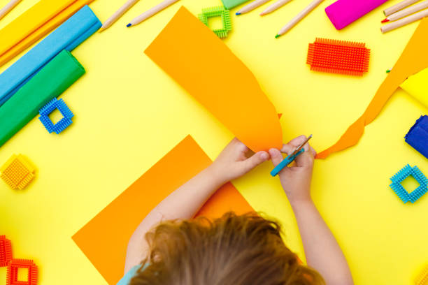 istock Child cutting coloured orange paper with scissors  on a table for some craftwork 1248569460