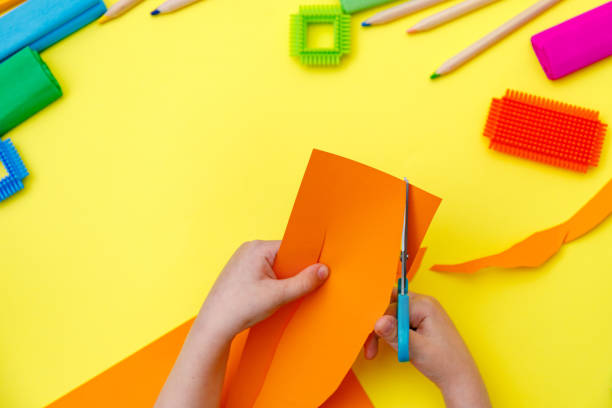 istock Child cutting coloured orange paper with scissors  on a table for some craftwork 1248569500