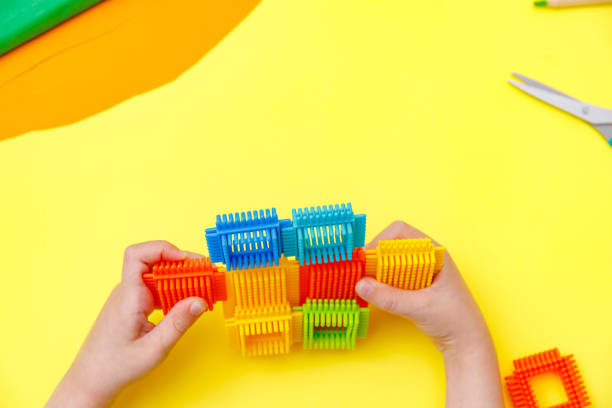 istock Top view on child's hands playing with colorful plastic bricks on yellow background. Boy building with plastic constructor. Education concept 1248569536