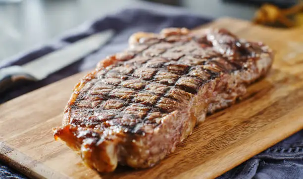 grilled new york strip steak resting on wooden cutting board shot with selective focus