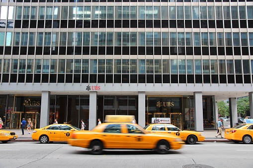 Yellow cab drives by UBS bank at Avenue of the Americas (6th Avenue), New York City.