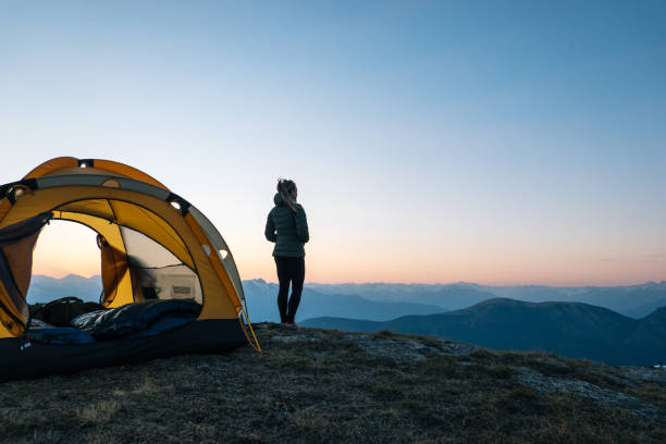 Young woman watches sunrise outside camping tent Sun rises over distant Swiss Alps camping stock pictures, royalty-free photos & images