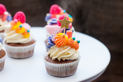 Chocolate cupcakes with cream cheese frosting, pinka and orange chewing marmalade, sweets and golden topper on dark background