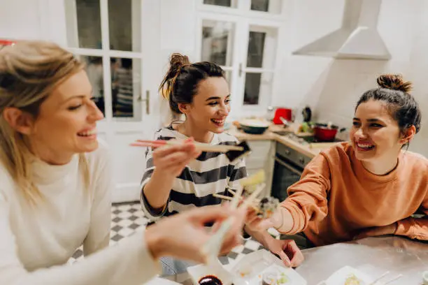 Photo of a group of friends eating traditional Japanese food in the kitchen and having a great time; enjoying in each other's company during dinner at home.