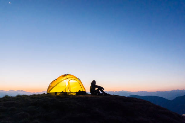 Young woman watches sunrise outside camping tent Sun rises over distant Swiss Alps simple living stock pictures, royalty-free photos & images