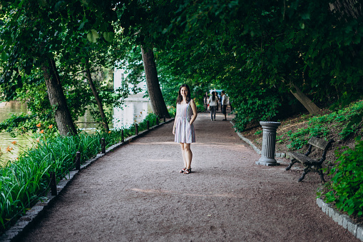 Sofia Park, Uman. Girl in a summer board on the alley of the park. Smiling brunette girl on a stone alley near the lake. Walk in the park, a large beautiful lake