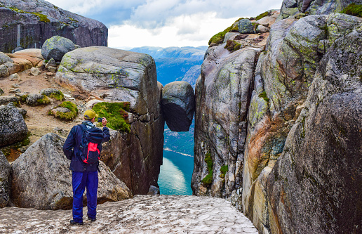 Tourist man takes a photo of the most dangerous stone in the world of Kjeragbolten. Kjeragbolten is a rock stuck at an altitude of 984 meters above Lysefjorden on mountain Kjerag, Norway.