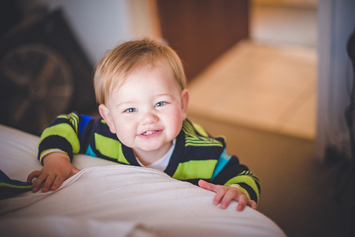 Cute Toddler smiling holding onto the bed.