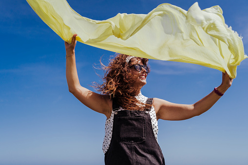 young caucasian woman outdoors playing with yellow scarf on a windy and sunny day. Lifestyle and summertime