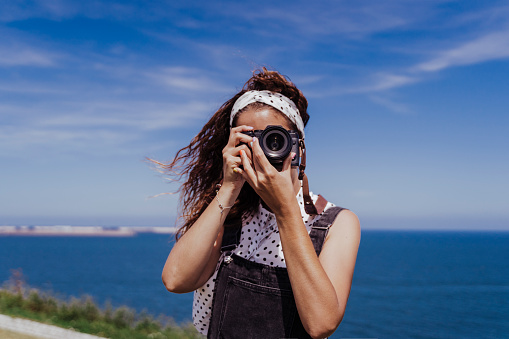 young caucasian tourist woman outdoors taking pictures with a reflex camera on a windy and sunny day. Lifestyle, travel and summertime