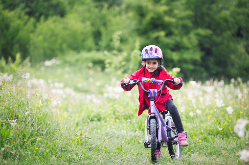 little girl rides a bike on a green meadow in nature.