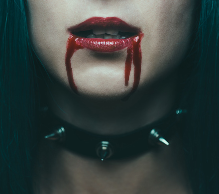 Beautiful vampire young woman with red lips in blood and necklace with spikes, close-up.
