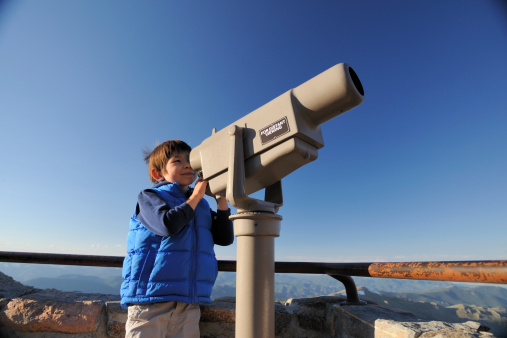 A closeup of shiny telescope by mesh wire fence with blur cityscape in the background