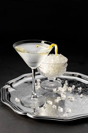 A cocktail shaker pours martini into a martini glass