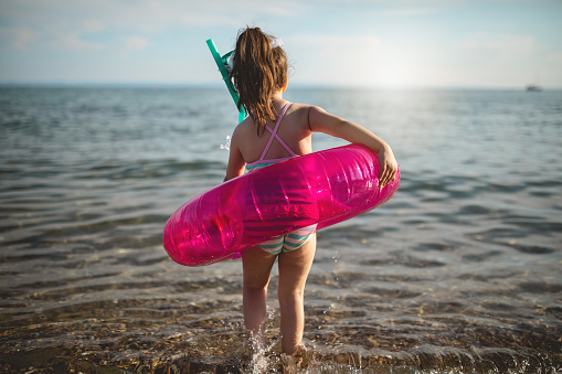 Little girl playing around with an inflatable ring on a beach in Greece during her summer vacation