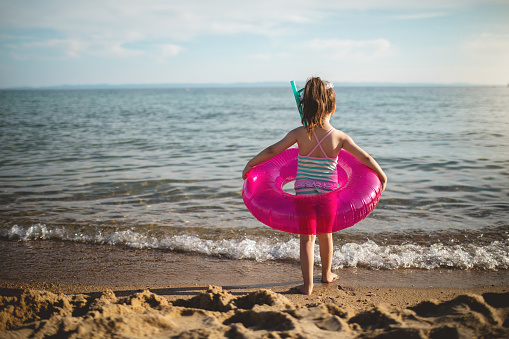 Little girl playing around with an inflatable ring on a beach in Greece during her summer vacation