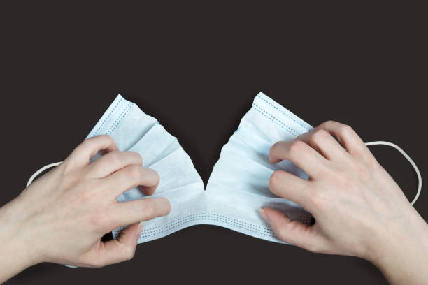 Hands tearing safety face mask. Isolated on dark gray background. Concept of protest against quarantine caused by COVID19 pandemic. stock photo