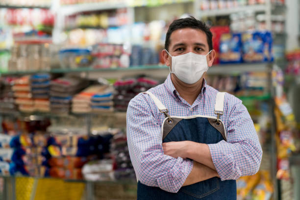 Business manager working at a convenience store wearing a facemask Portrait of a business manager working at a convenience store wearing a facemask to avoid the coronavirus and looking at the camera with arms crossed - pandemic lifestyle concepts convenience store photos stock pictures, royalty-free photos & images