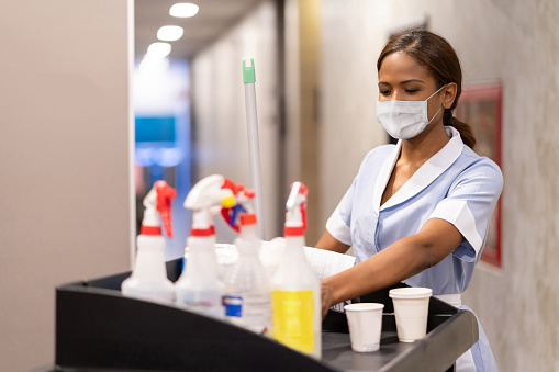 Latin American Maid working at a hotel doing room service wearing a facemask and pushing a cart â COVID-19 pandemic lifestyle concepts