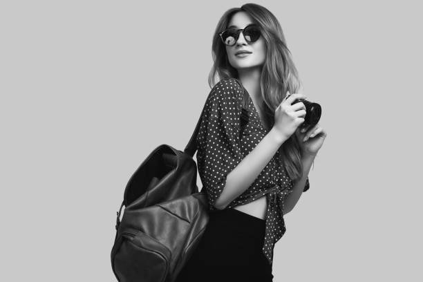 Portrait of young beautiful woman with backpack and camera ready to travel. Smiling student girl going on a vacation. Isolated on gray background.