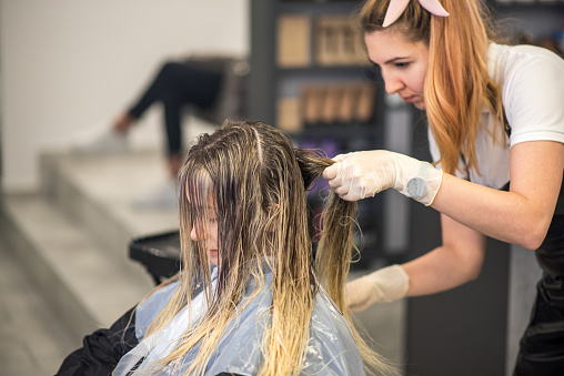 Pretty young woman, teenage girl, having her hair highlighted, dyed and washed at the hair salon. Reopening business, hair salon after coronavirus, Covid-19 quarantine.