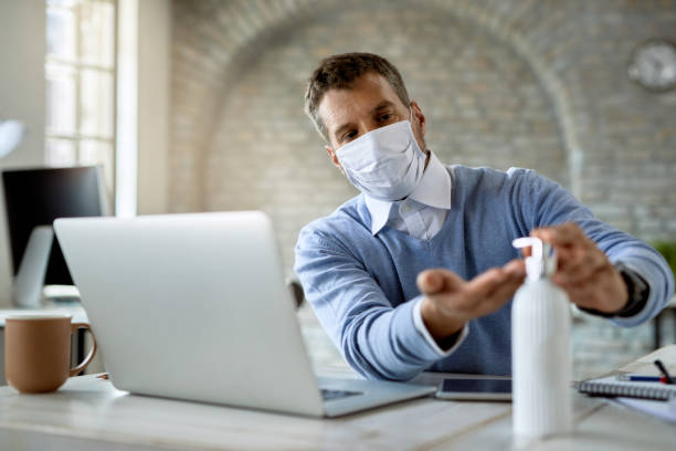istock Male entrepreneur with protective face mask using hand sanitizer in the office. 1248616773